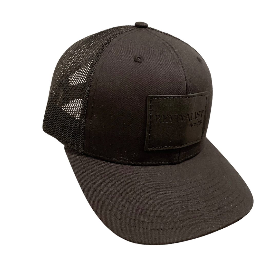 Revivalist Design hat. Black trucker hat with black leather patch embossed with 