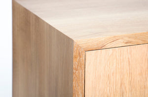 detailed photo of the mitered edge on the cascade reserve desk in cerused white oak. Shows the miter that joins that left leg to the desktop and the small distance between the desk frame and the door that hides the storage shelves.