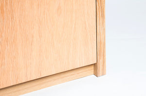 Detail photo of the bottom toe kick of the cascade reserve desk. It shows the area where the bottom of the door storage area meets the bottom structural portion of the desk design. The finish is cerused white oak.