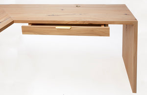 Detailed photo of the drawer slightly pulled out on the minimalist cascade desk. The miter that connects the desktop to the right leg can be seen. The brass desk handle can be seen. the brass grommet for electrical cord management can be seen.
